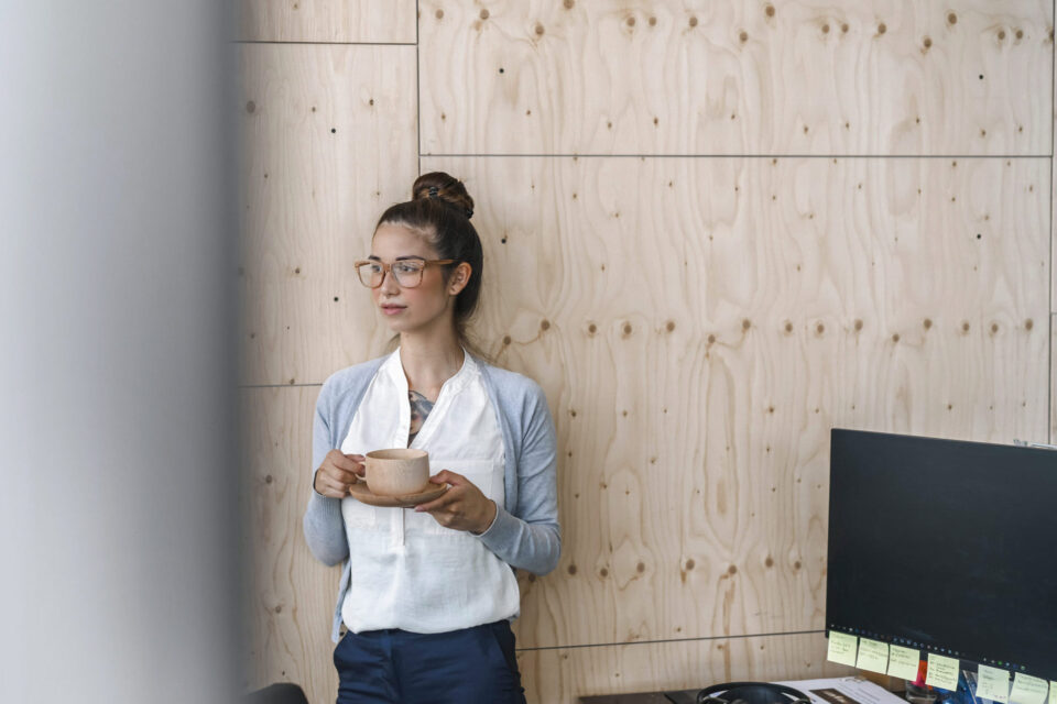 Junge Frau arbeitet in einem modernen Büro, macht eine Pause und trinkt Kaffee aus einer Holztasse